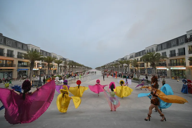 Dancers in colorful carnival costumes perform on a plaza lined with shophouses and palm trees in Quy Nhon.
