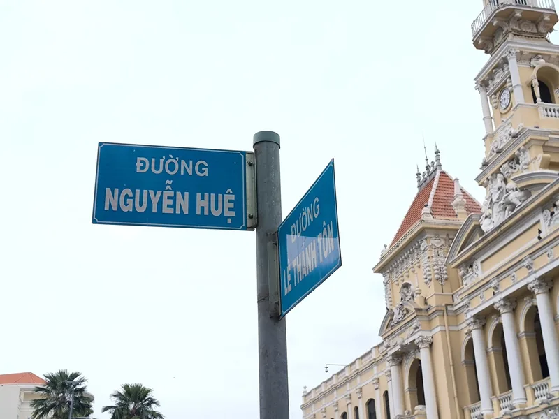 Street signs for Nguyen Hue and Le Thanh Ton streets stand near the historic City Hall building in Ho Chi Minh City.
