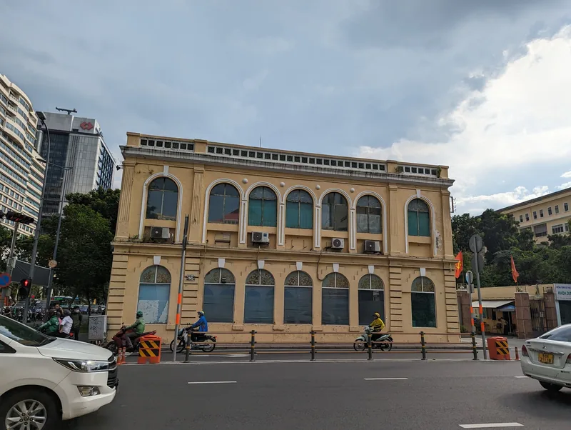 A yellow French colonial building with arched windows stands along a busy street in Ho Chi Minh City's District 1.