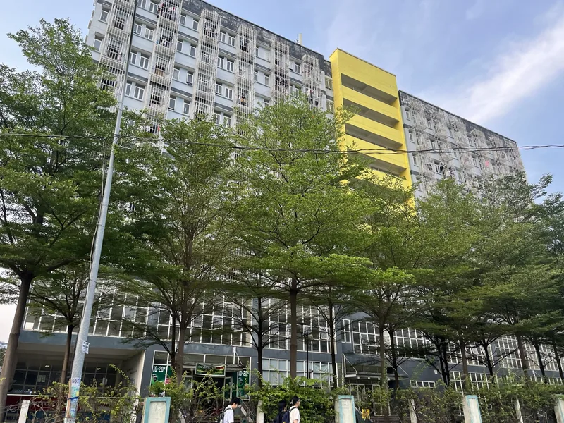 A tall apartment block with barred balconies and a bright yellow stairwell stands behind trees in Ho Chi Minh City.