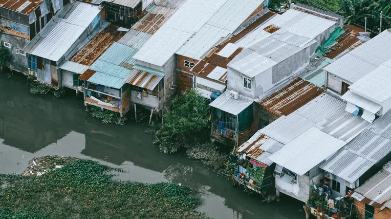 Aerial view of rusty tin-roofed houses on stilts along a murky canal in Ho Chi Minh City.