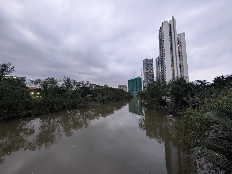 High-rise towers rise beyond a mangrove-lined canal in Ho Chi Minh City's District 7 under overcast skies.