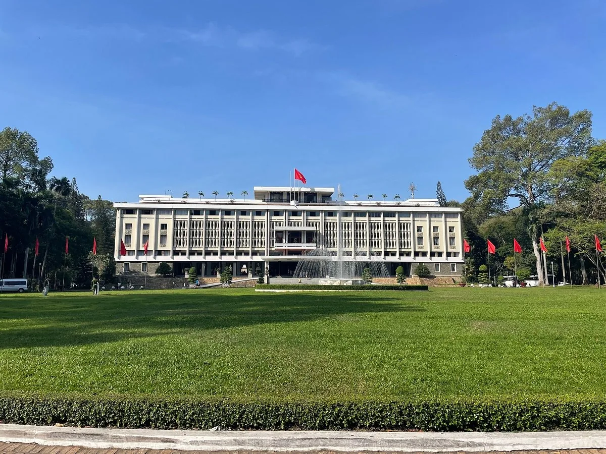 The Independence Palace facade with a fountain and green lawn under a clear sky in Saigon.