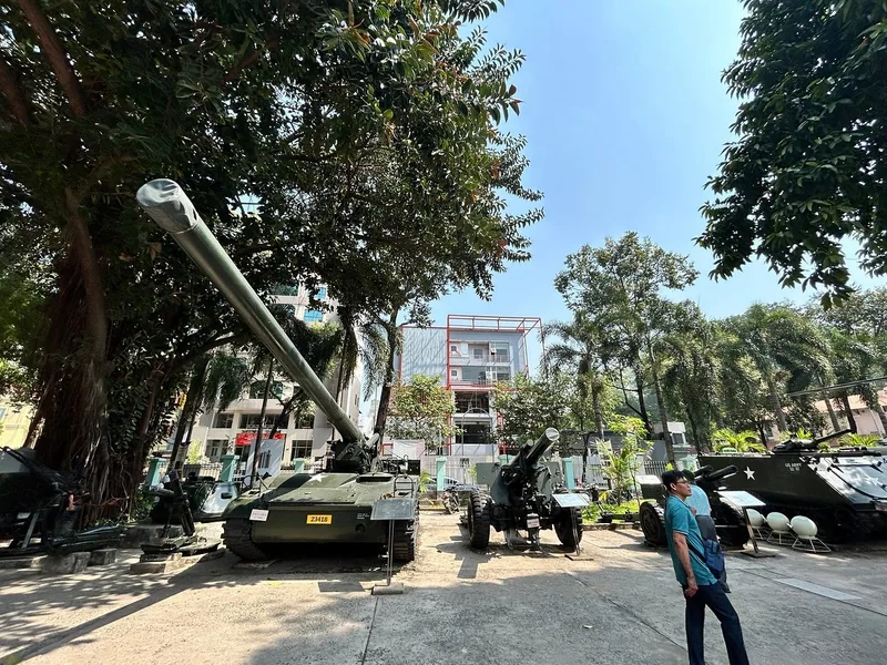 Tanks and artillery on display in a shaded outdoor courtyard, likely the War Remnants Museum in Saigon.