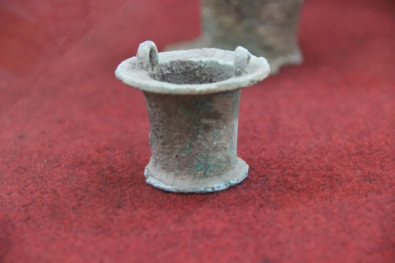 A small corroded bronze Dong Son-era object displayed on red fabric in a museum in Ho Chi Minh City.