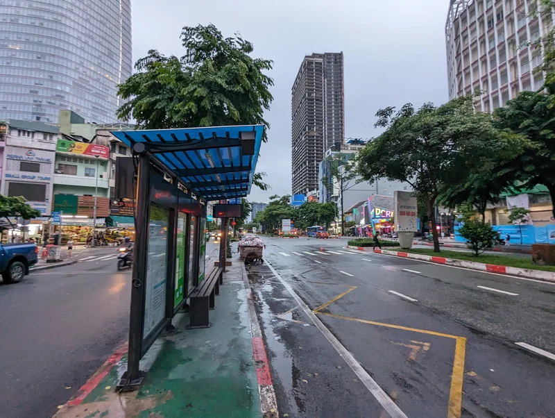 A quiet bus stop stands beside a wet street lined with high-rises in Ho Chi Minh City's District 1.