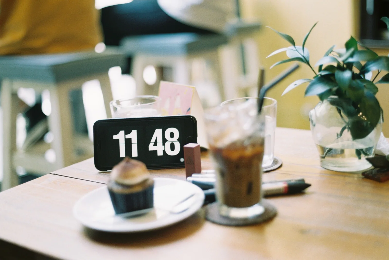 A café table in Ho Chi Minh City with iced coffee, a cupcake, and a phone showing the time.