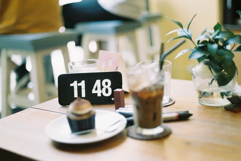 A café table in Ho Chi Minh City with iced coffee, a cupcake, and a phone showing the time.