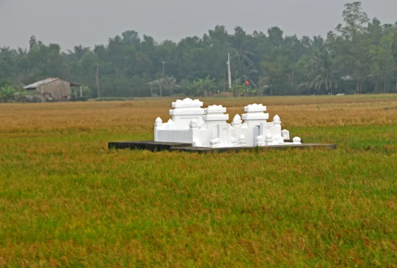 A small white ornate tomb sits amid green and golden rice fields on the outskirts of Ho Chi Minh City.