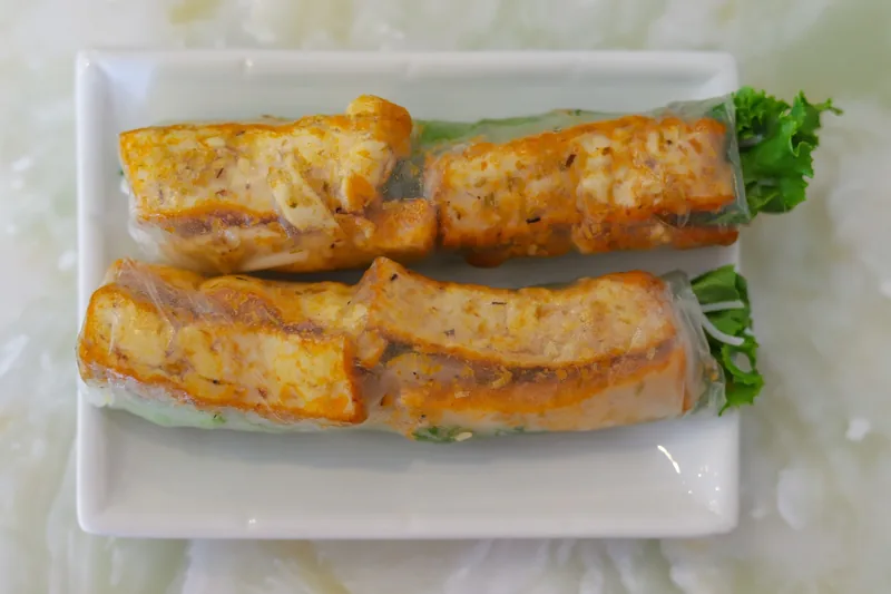 Two Vietnamese vegetarian fresh spring rolls filled with grilled tofu and herbs served on a white plate.