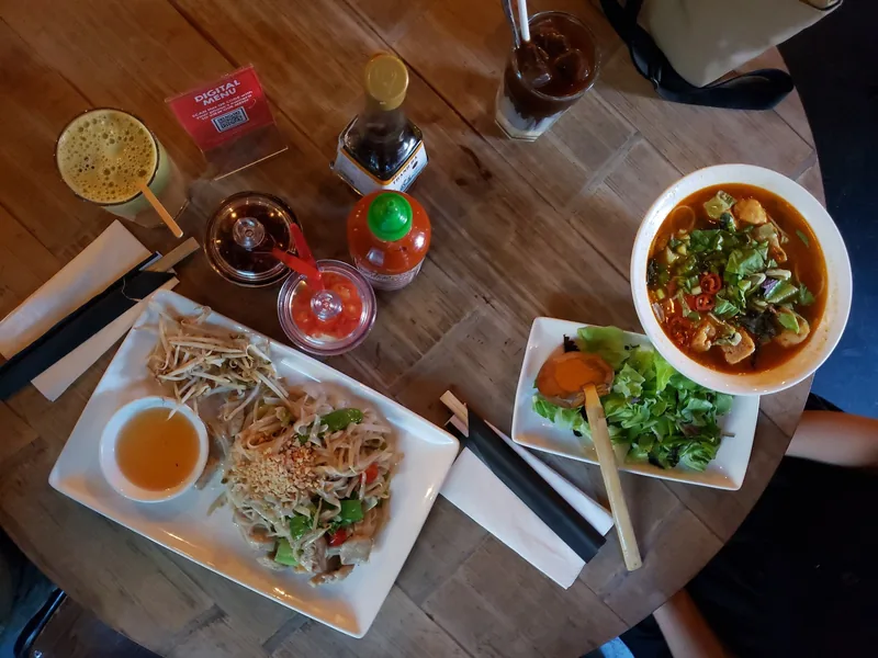 An overhead view of a wooden table set with pho, salad, noodle salad, and drinks at a Vietnamese restaurant.