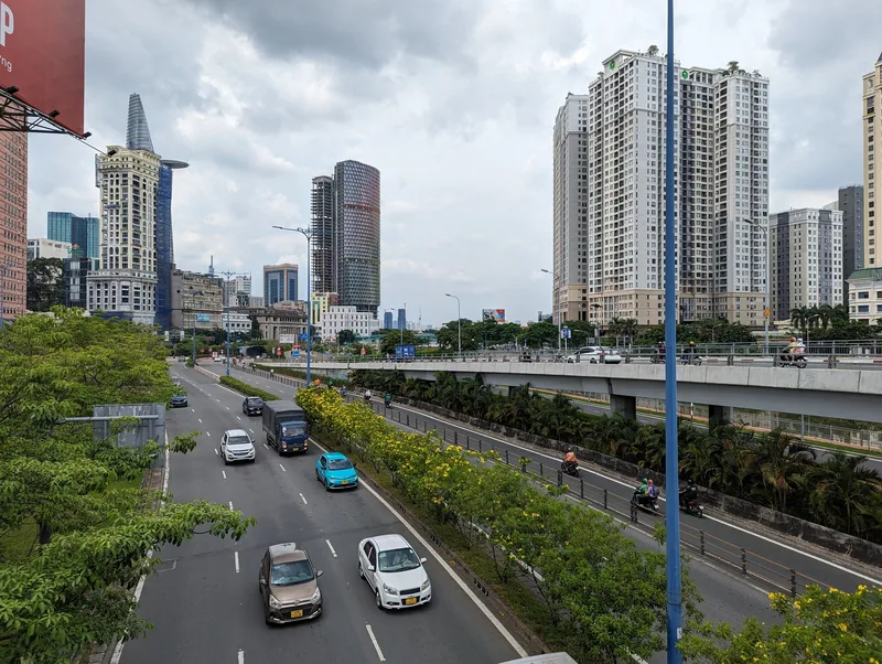 Traffic flows along a wide boulevard beneath skyscrapers and the Bitexco tower in downtown Ho Chi Minh City.