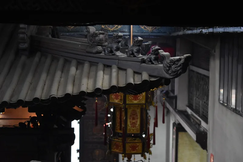 Ornate tiled roof with dragon figurines and a hanging lantern at a Chinese temple in Ho Chi Minh City
