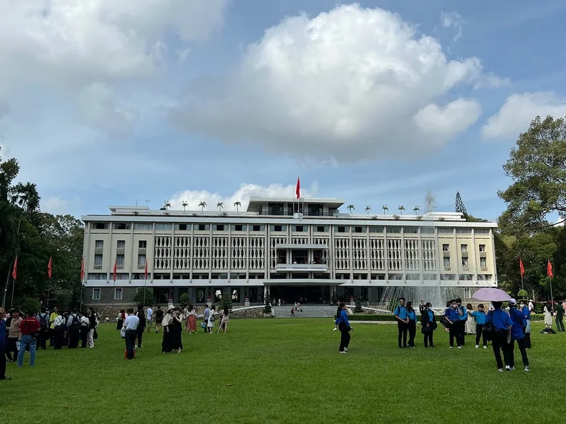 Visitors gather on the lawn in front of the Independence Palace in Saigon under a bright sky.