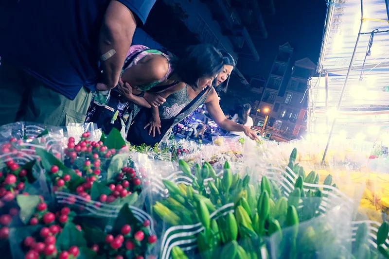 Shoppers browse fresh berries and lily buds at a bustling night flower market stall in Saigon.