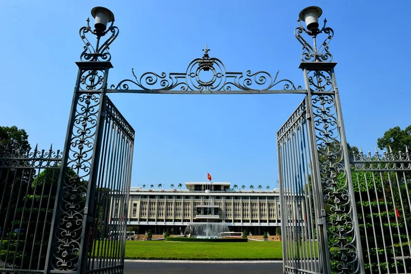 Ornate iron gates open to reveal the Reunification Palace and fountain in Ho Chi Minh City.