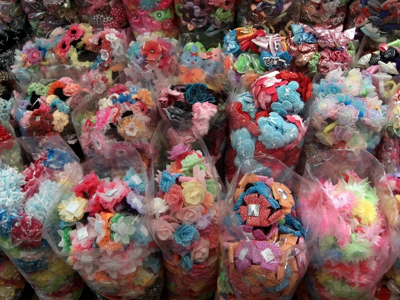 Bundles of colorful fabric flower hair accessories packed in plastic at a Ho Chi Minh City market stall.