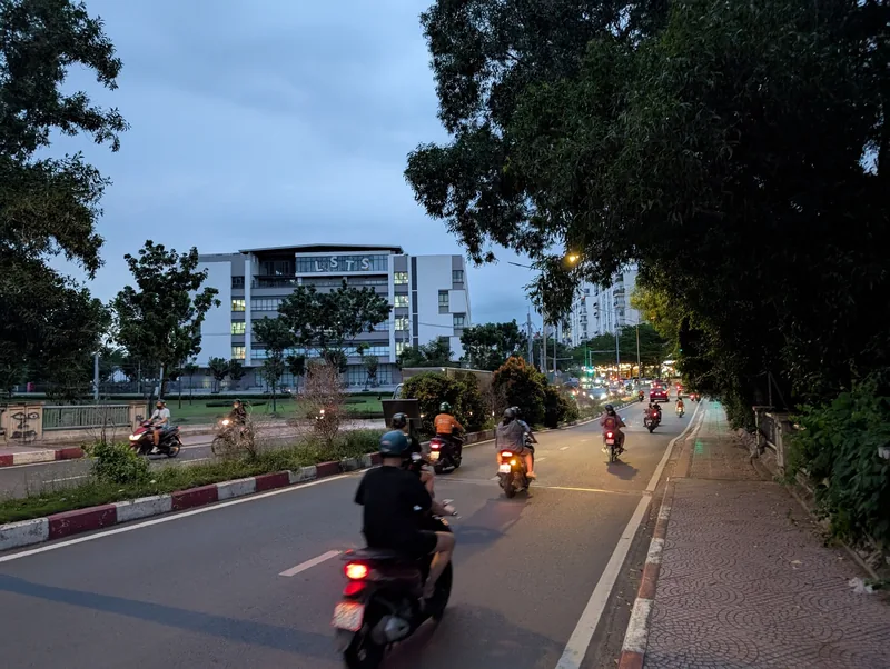 Motorbikes ride along a tree-lined street at dusk in Ho Chi Minh City's District 7.