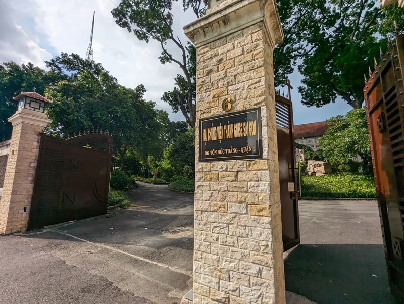 Stone gate entrance with signage leads to a tree-lined driveway in District 1, Ho Chi Minh City.