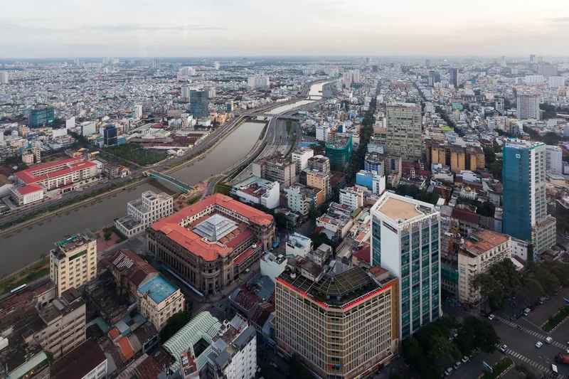 Aerial view of Ho Chi Minh City skyline with a winding canal and dense mix of low-rise and high-rise buildings.