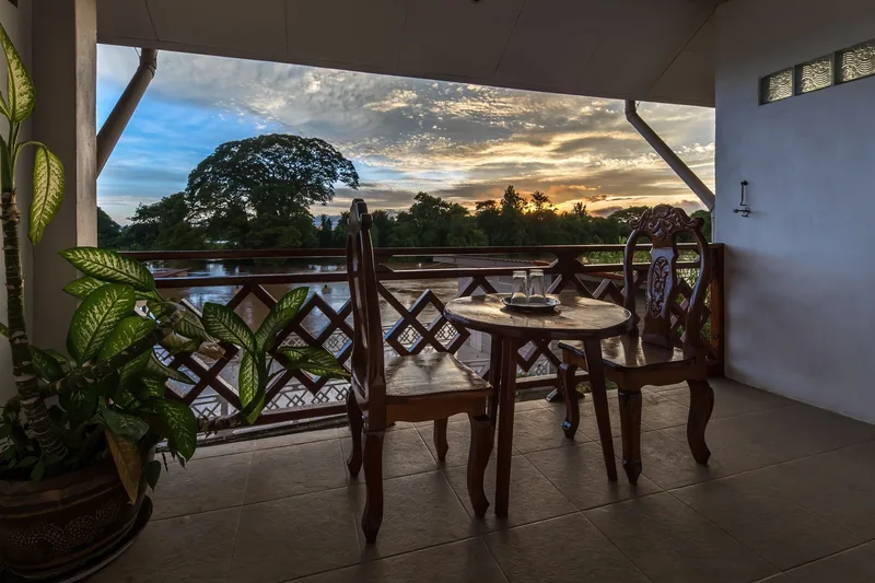 A wooden table and chairs on a riverside balcony overlook the Mekong River at sunset in Si Phan Don.