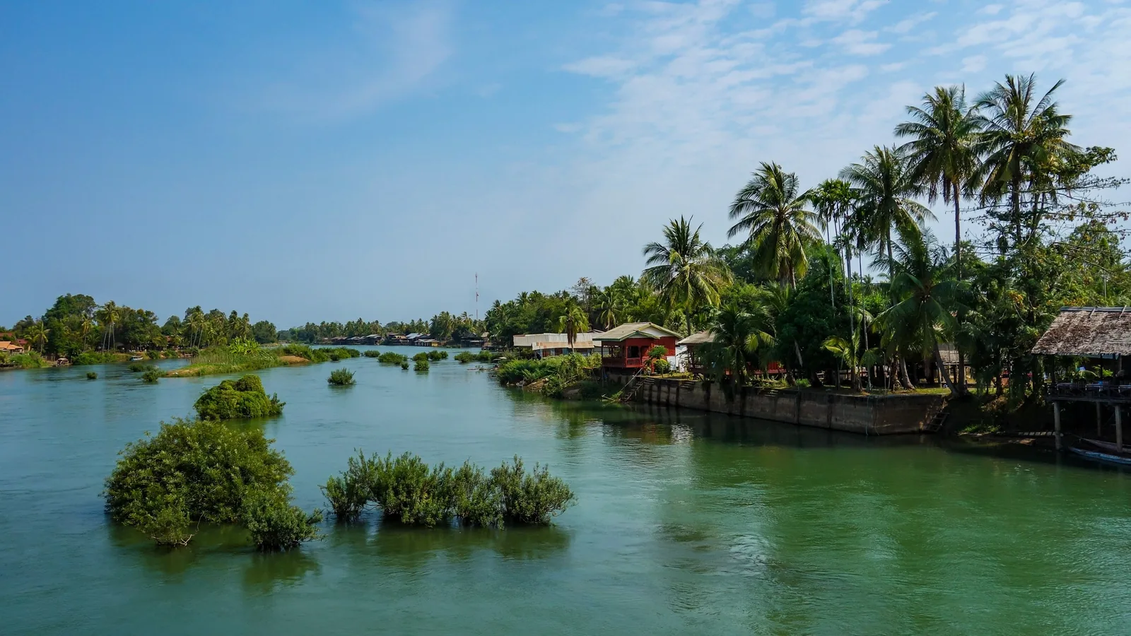 Wide river channel with palm-lined banks and small huts in Si Phan Don, Laos