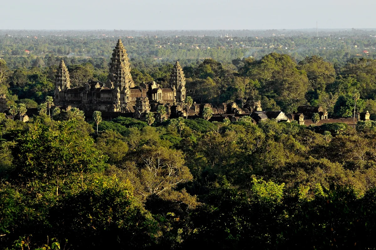 The towering spires of Angkor Wat rise above a dense green forest canopy near Siem Reap.