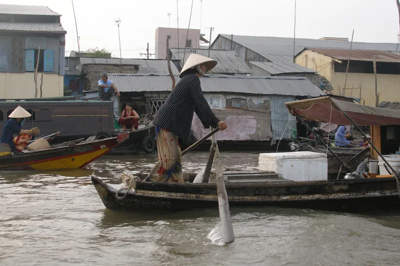A woman in a conical hat rows a wooden boat through the floating market on the river in Can Tho.