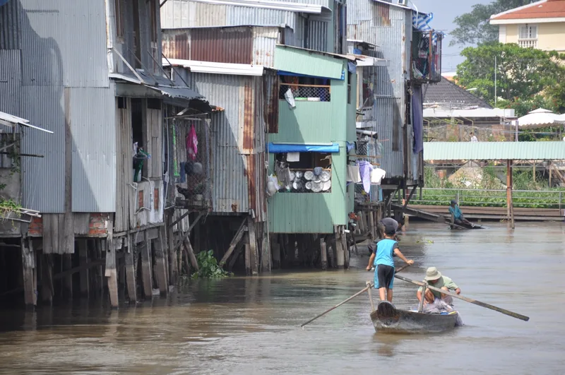 A small rowboat carries people past corrugated metal stilt houses along the river in Chau Doc.