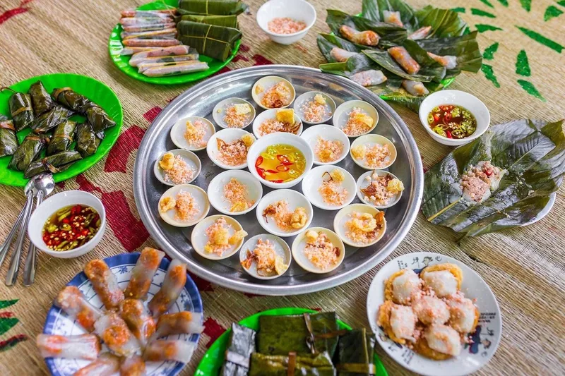 A spread of traditional Hue dishes including steamed rice cakes, spring rolls, and dipping sauces arranged on a woven mat.