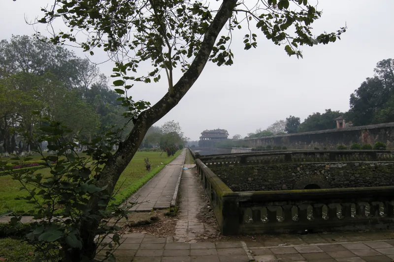A stone pathway runs beside old moat walls with a distant gate tower at the Imperial City of Hue.