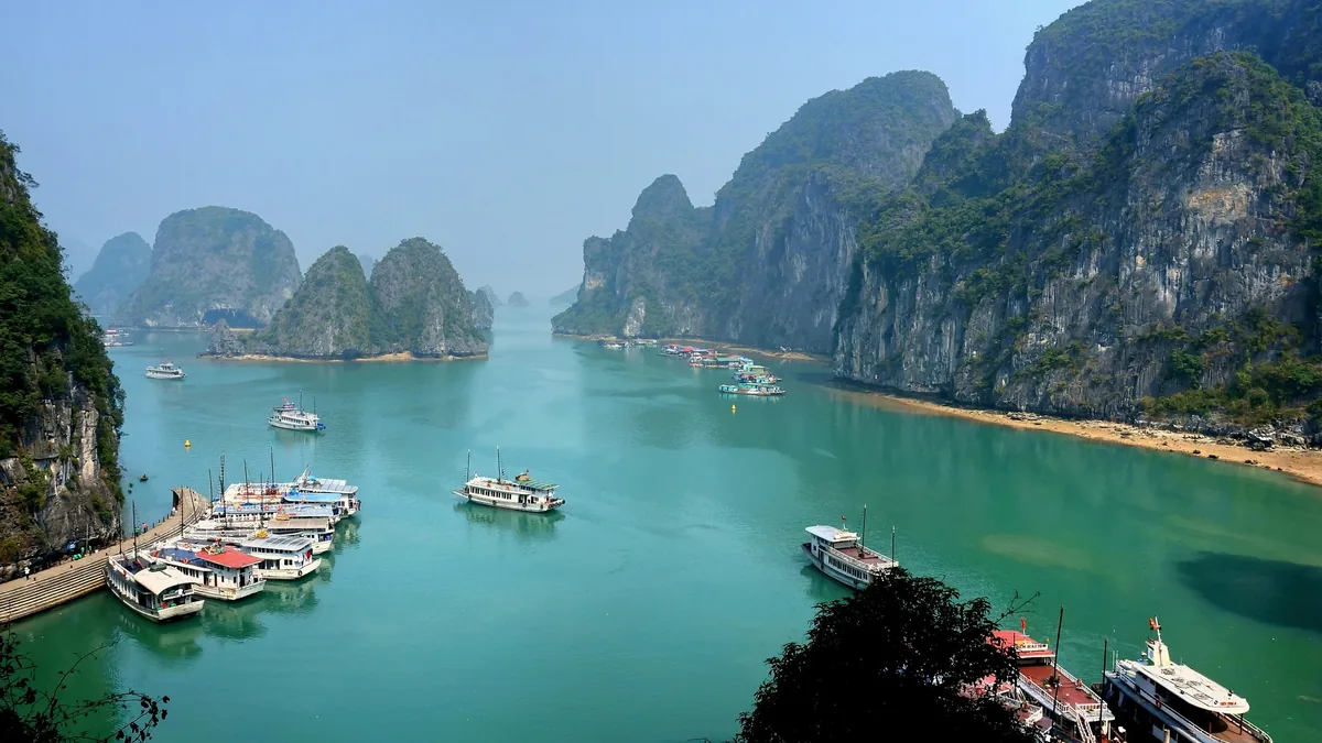 Tour boats dot the emerald waters of Ha Long Bay, surrounded by towering limestone karsts.