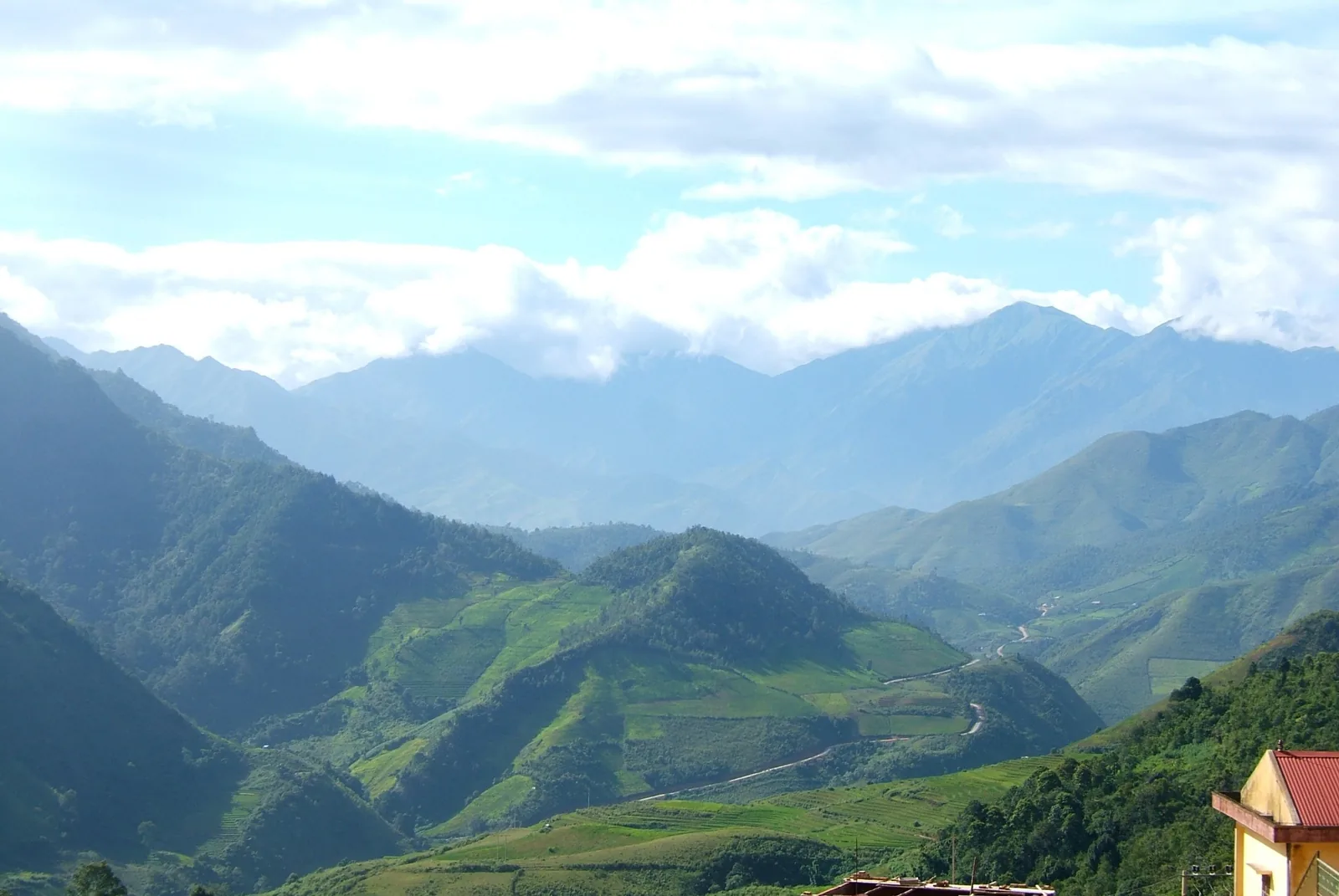 Layered green mountain ridges and a winding road stretch through the valley near Mu Cang Chai, Yen Bai province.