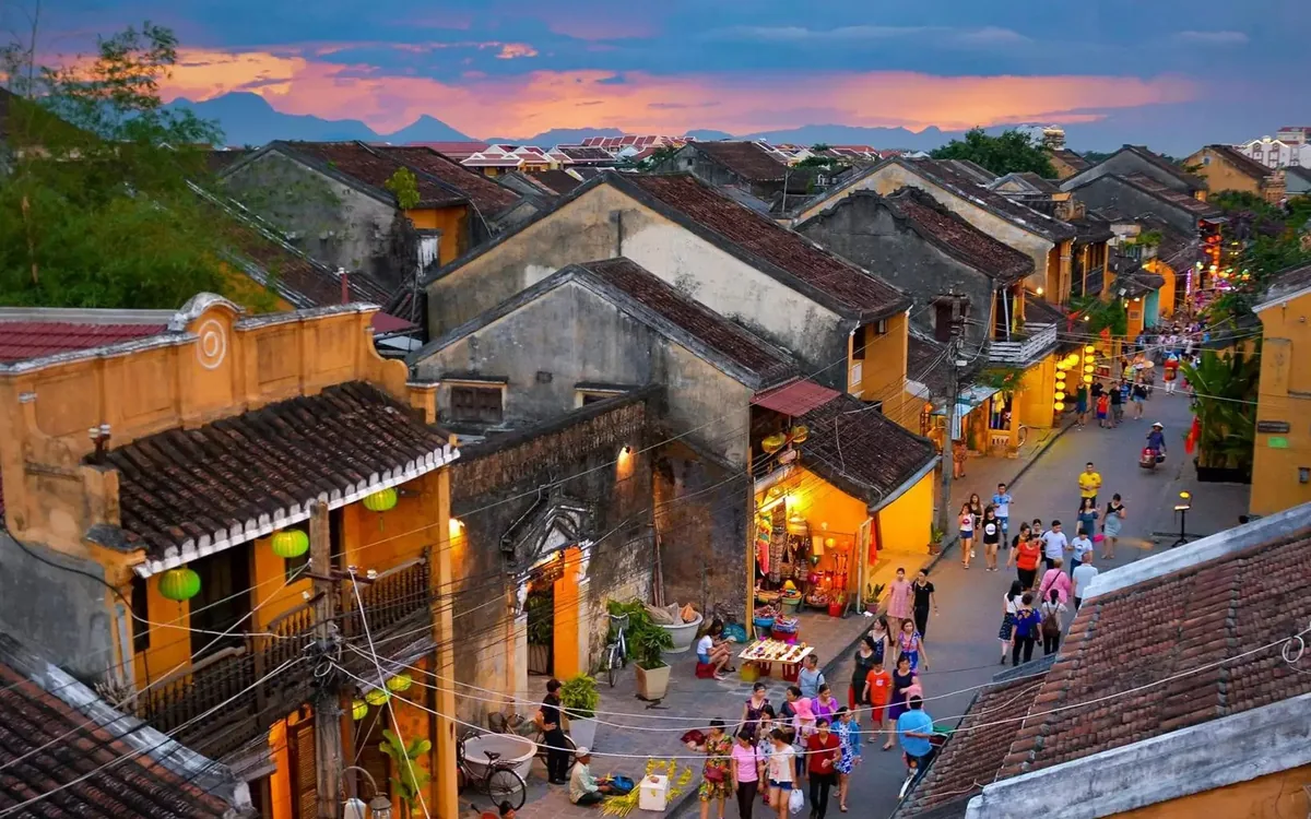 Aerial view of Hoi An's old town rooftops and lantern-lit streets crowded with visitors at dusk.