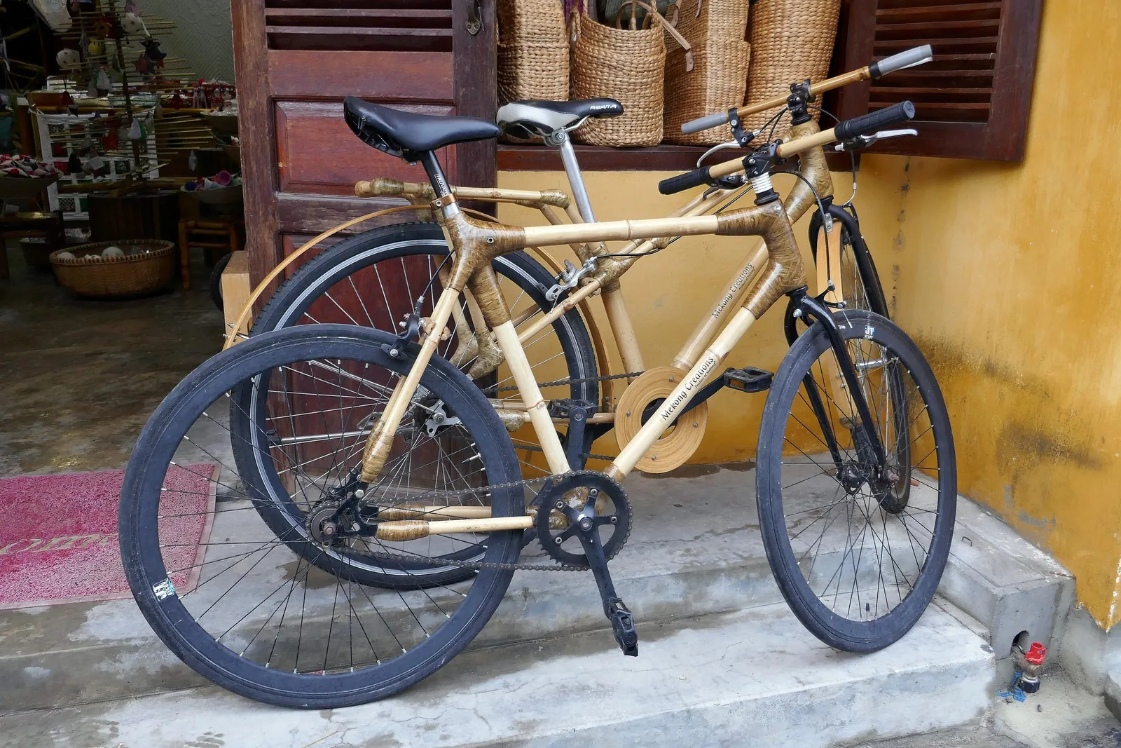 Two bamboo-frame bicycles parked against a yellow wall in Hoi An.