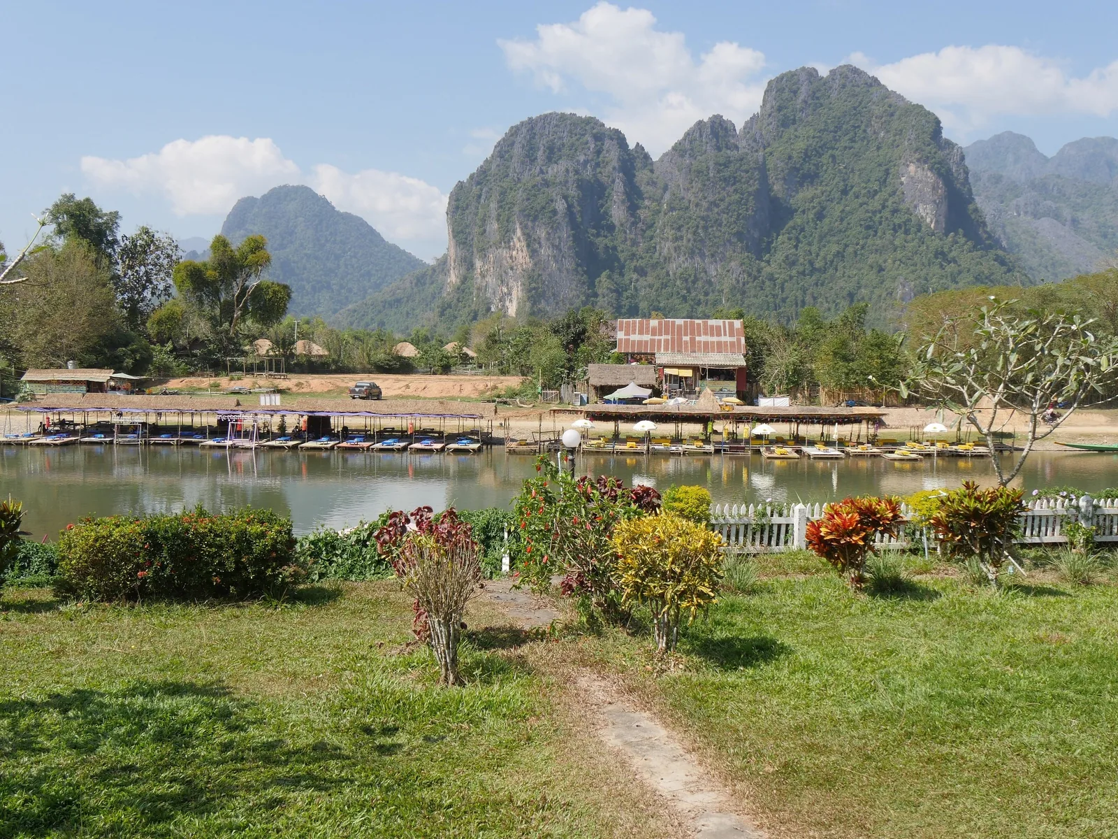 Limestone karst mountains rise behind a boat dock and garden at a riverside resort in Vang Vieng.