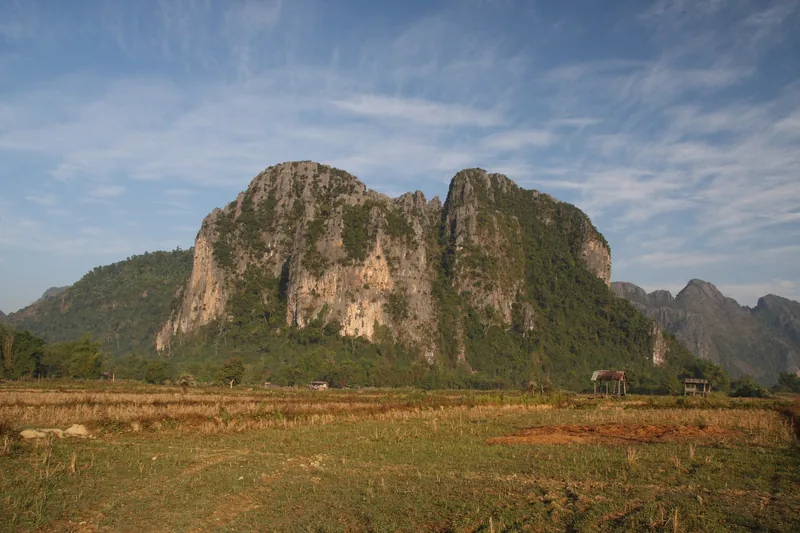 Rugged limestone karst mountains rise above dry rice fields near Vang Vieng, Laos.