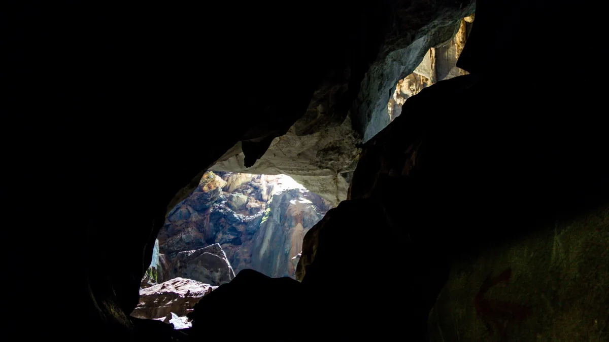 Sunlight streams through a cave opening revealing rocky cliffs outside near Vang Vieng, Laos.