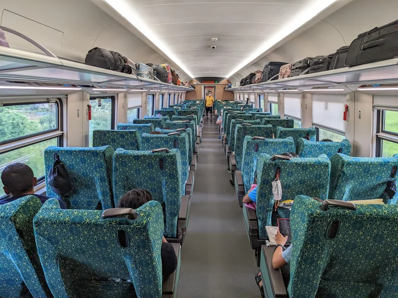 Rows of teal seats fill the first-class carriage of a Laos-China Railway train near Vientiane, with luggage stowed overhead.