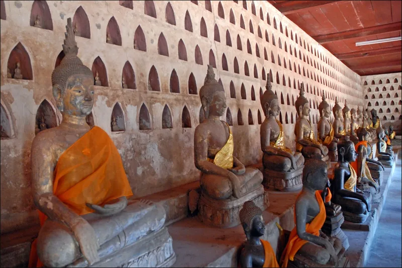 Rows of seated Buddha statues draped in orange cloth line the cloister wall at Wat Sisaket in Vientiane.