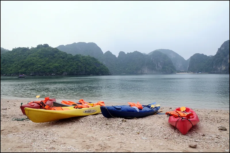 Kayaks and life jackets rest on a beach with limestone karsts rising from Lan Ha Bay.