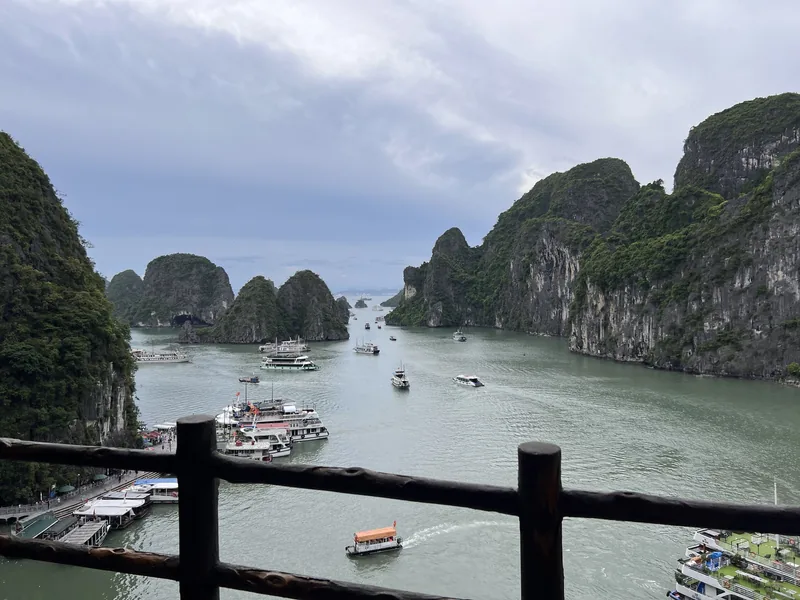 Tour boats cruise among limestone karst islands in Ha Long Bay, viewed from an elevated wooden railing.