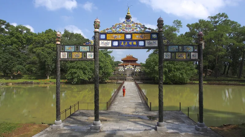 A woman in orange crosses a bridge through an ornate gate leading to Minh Mang's imperial tomb in Hue.