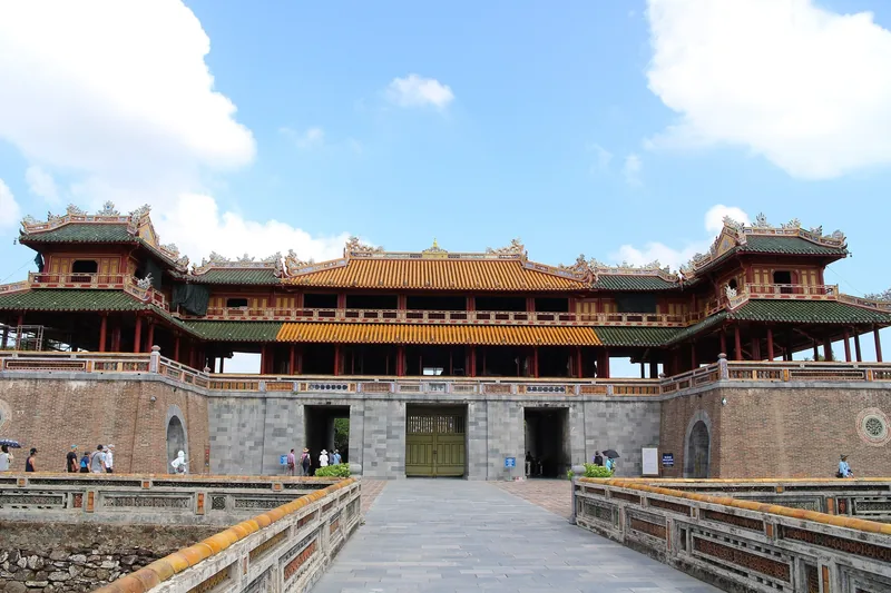 The Meridian Gate of the Hue Citadel rises with tiered yellow-tiled roofs above stone walls under a blue sky.