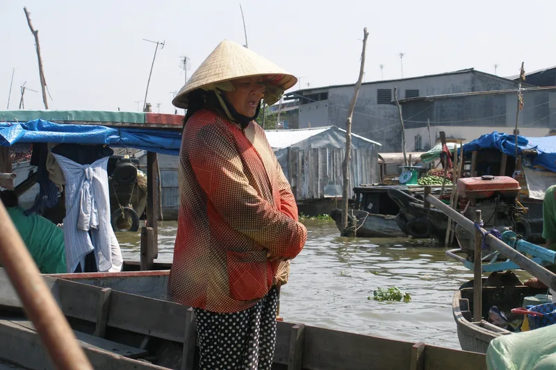 A woman in a conical hat stands on a boat at the floating market in Can Tho, Vietnam.