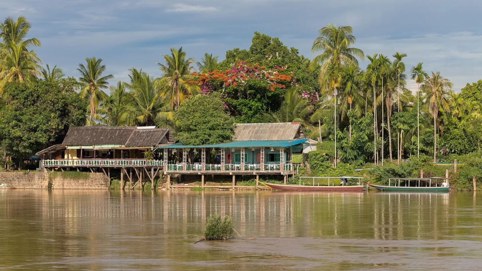 Stilt wooden houses and long-tail boats line the riverbank of Don Khon in Si Phan Don, Laos.