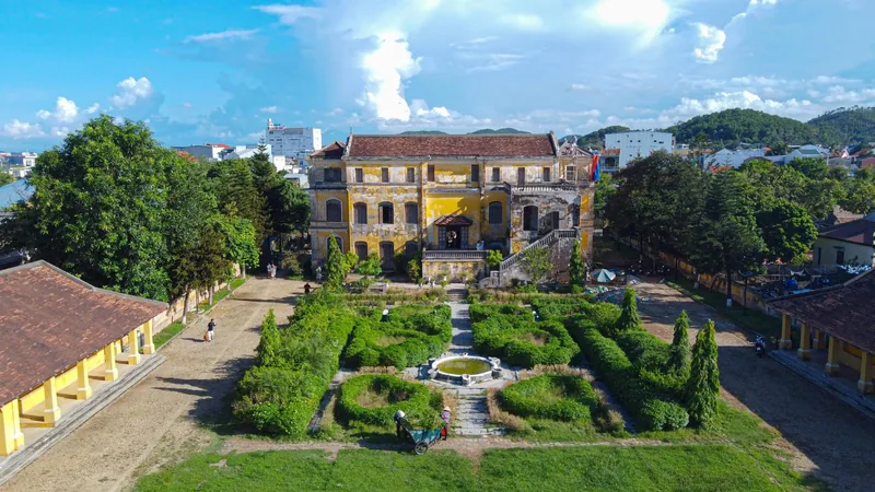 Aerial view of a yellow French colonial villa with a manicured garden and fountain in Hue.