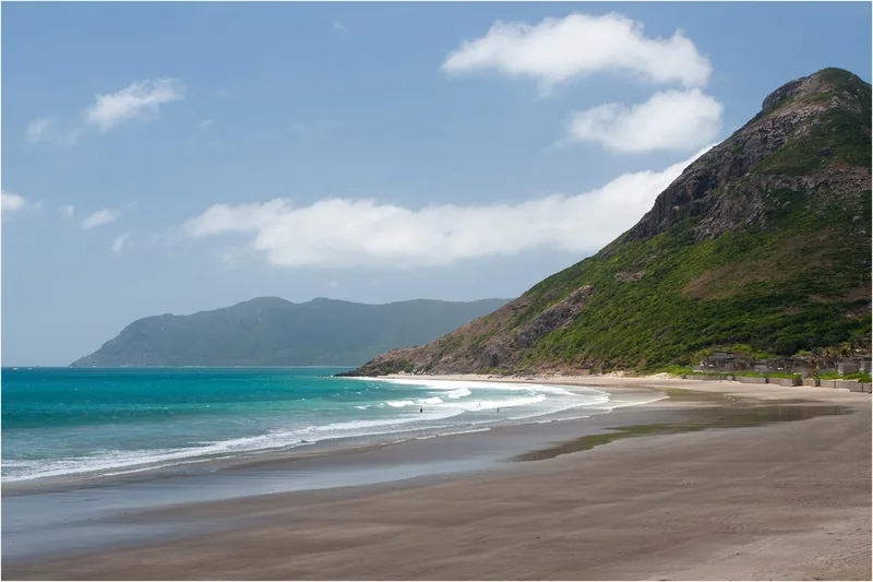 A wide sandy beach curves beneath green mountains along the turquoise coast of Con Dao.