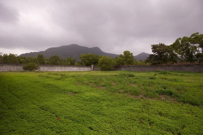 A stone perimeter wall surrounds a grassy field with misty mountains behind it at Con Dao prison site.