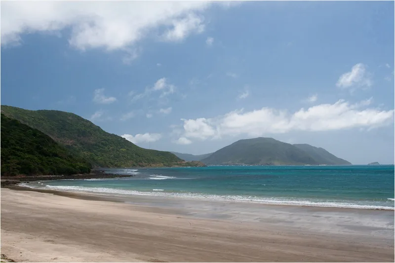 An empty sandy beach curves along turquoise water beneath green hills on Con Dao island.